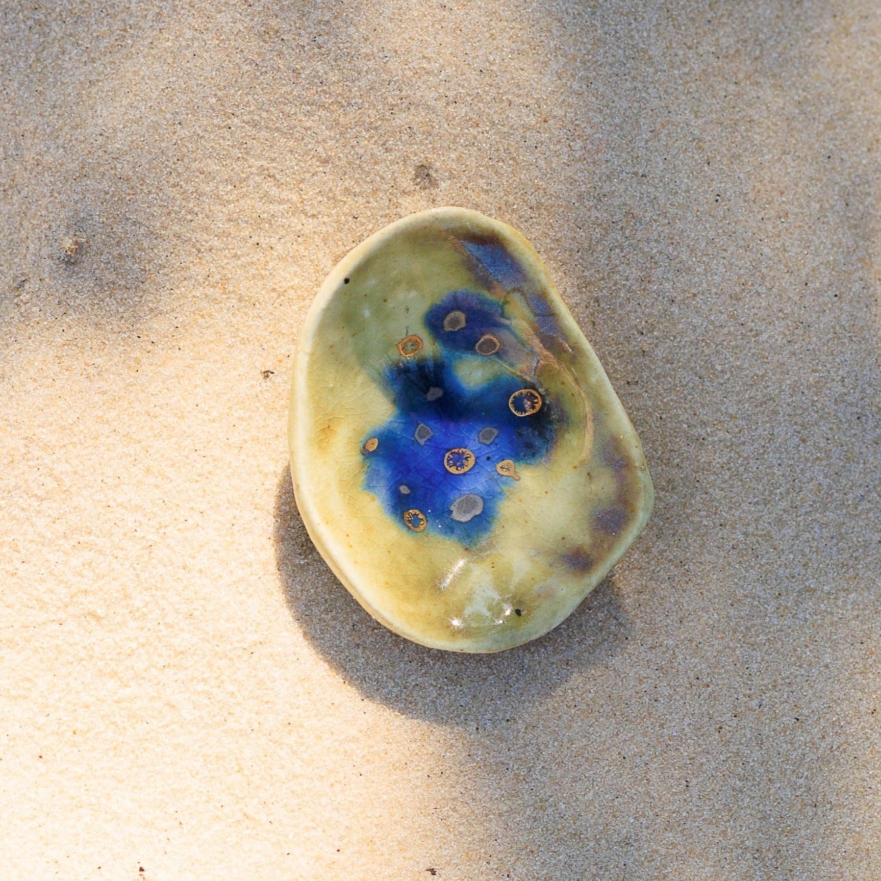 Brinco de porcelana oval de bordas irregulares e levemente concavo, cor verde oliva claro e azul, com pintas douradas